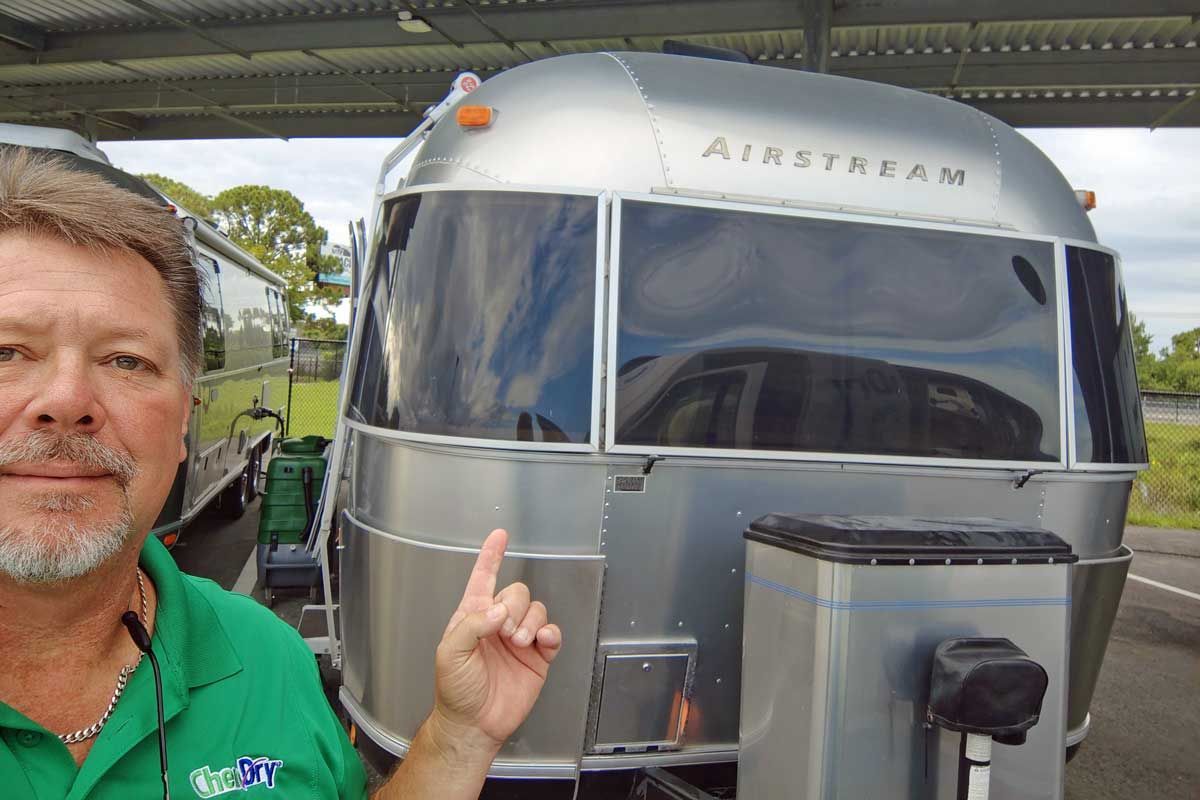 Roger from CHem-Dry Space Coast points at shiny silver Airstream trailer.