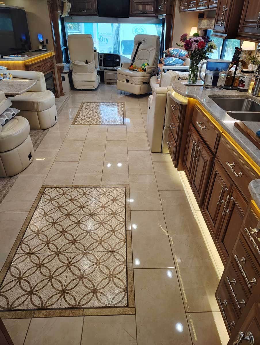 Interior view of a luxury RV with tile floors, wood cabinets, and cream-colored seating.