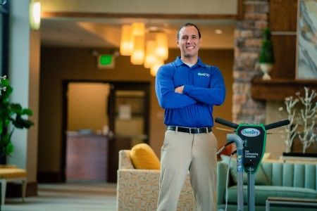 A smiling Chem-Dry technician stands by a floor cleaning machine in a lobby.