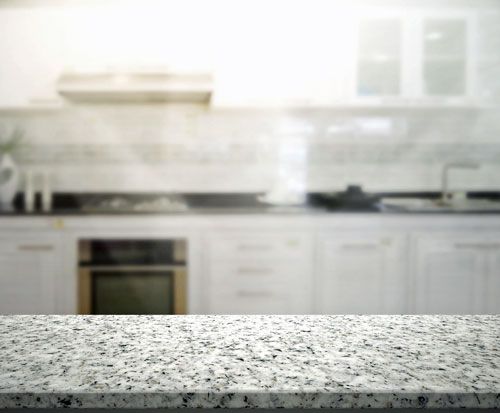 Granite countertop in front of a blurred white kitchen with oven and cabinets.