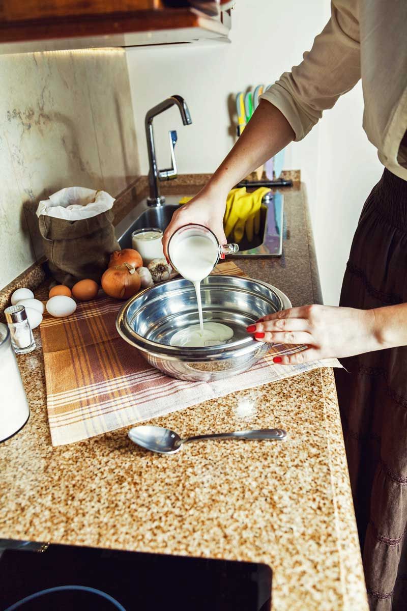 Woman pours liquid into a bowl on a kitchen counter.