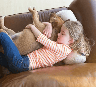 A young girl in striped shirt hugs a brown dog on a leather couch, both resting peacefully.