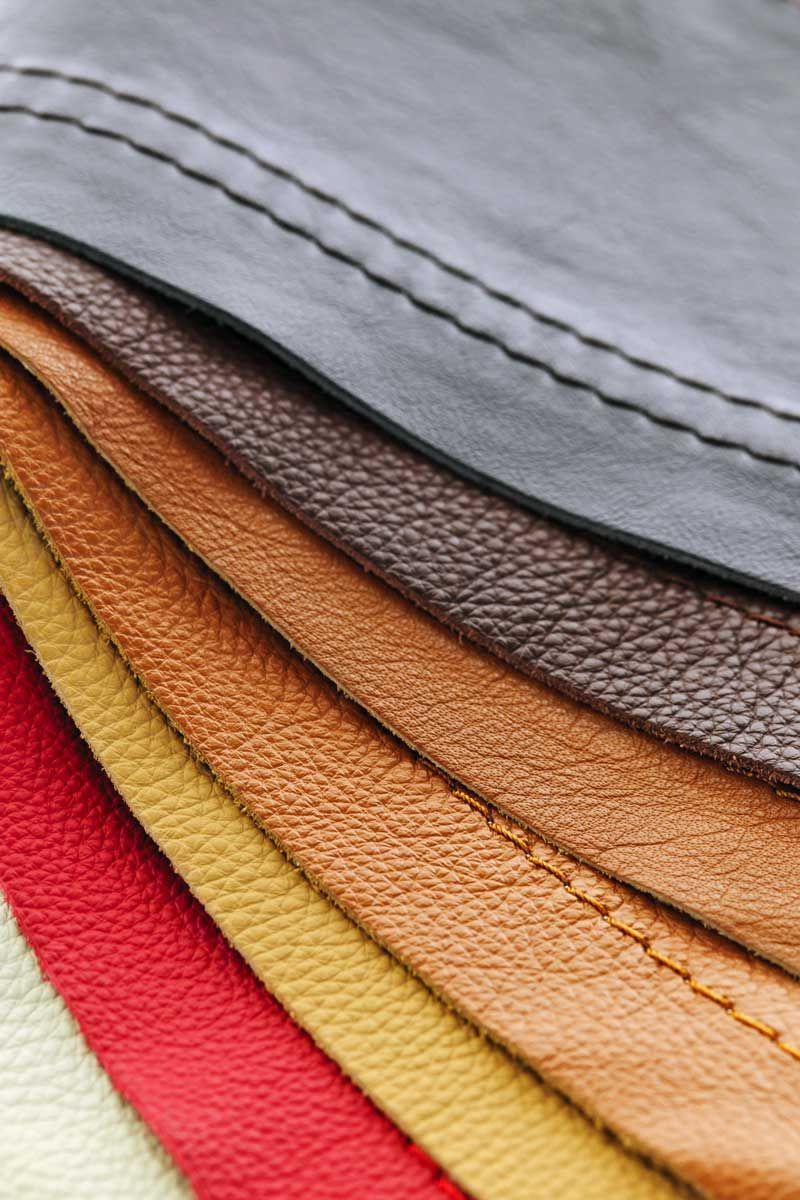 Close-up of a stack of leather swatches in shades of red, yellow, brown, and gray with stitched edges.