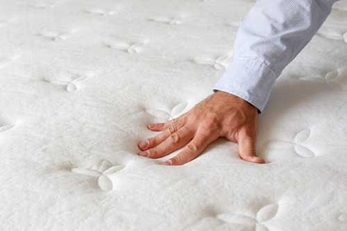 Hand presses down on a white, tufted mattress.