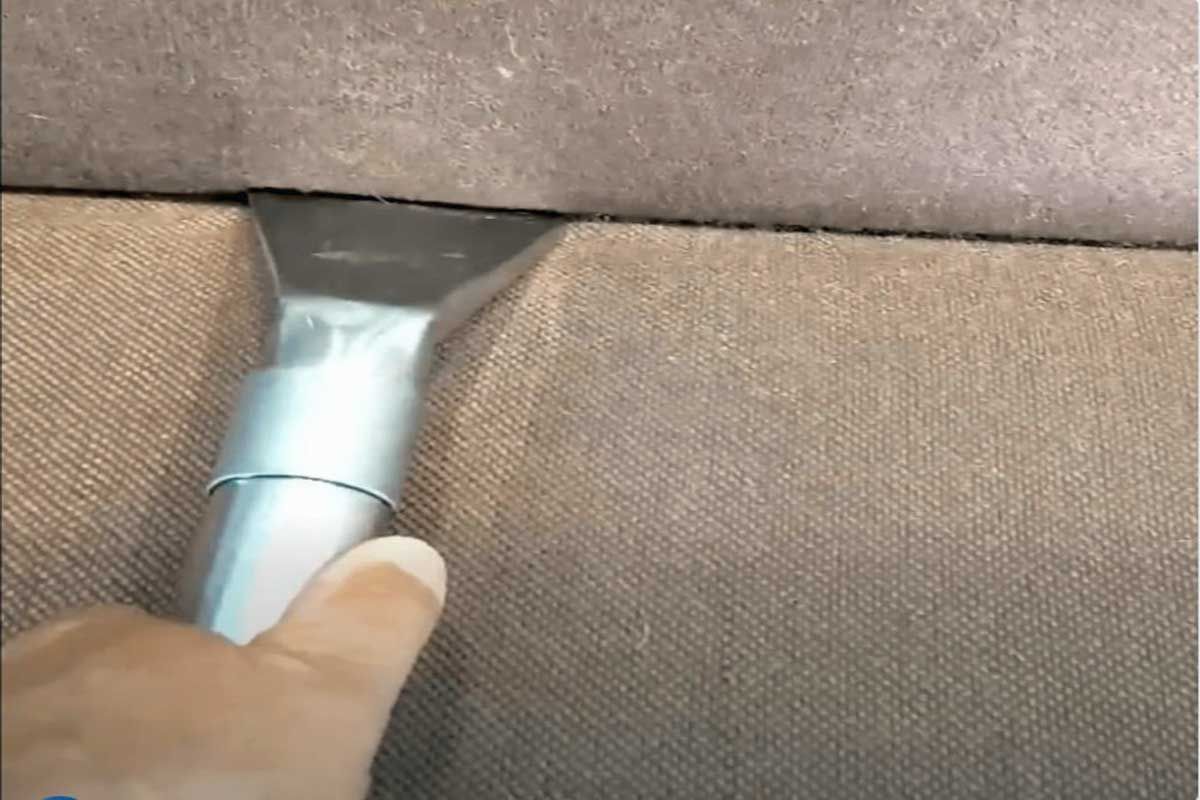 Hand vacuuming a brown sofa, cleaning a crevice.
