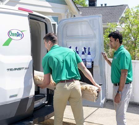 Two men from Chem-Dry unloading a rug from a white van. One carries the rug, while the other holds the van door.