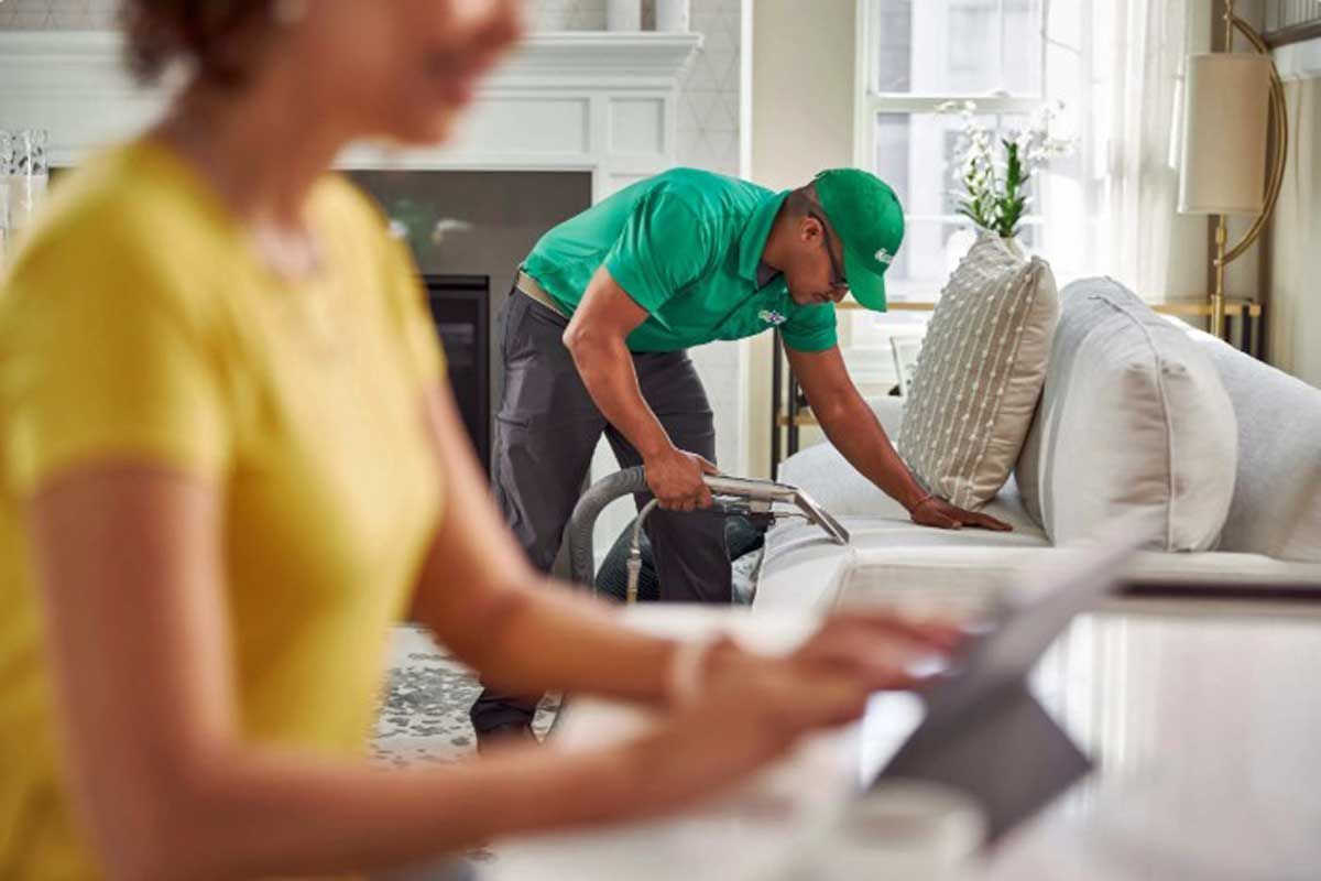 A Chem-Dry technician is vacuuming the sofa in the living room.