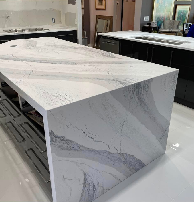 Kitchen island with white marble-like countertop and black cabinets. Undercounter shelving.