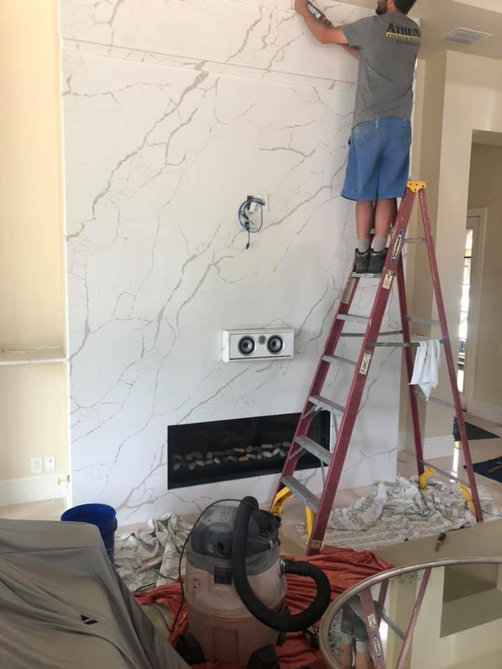 Man on a ladder installing white marble wall above a fireplace, construction site.