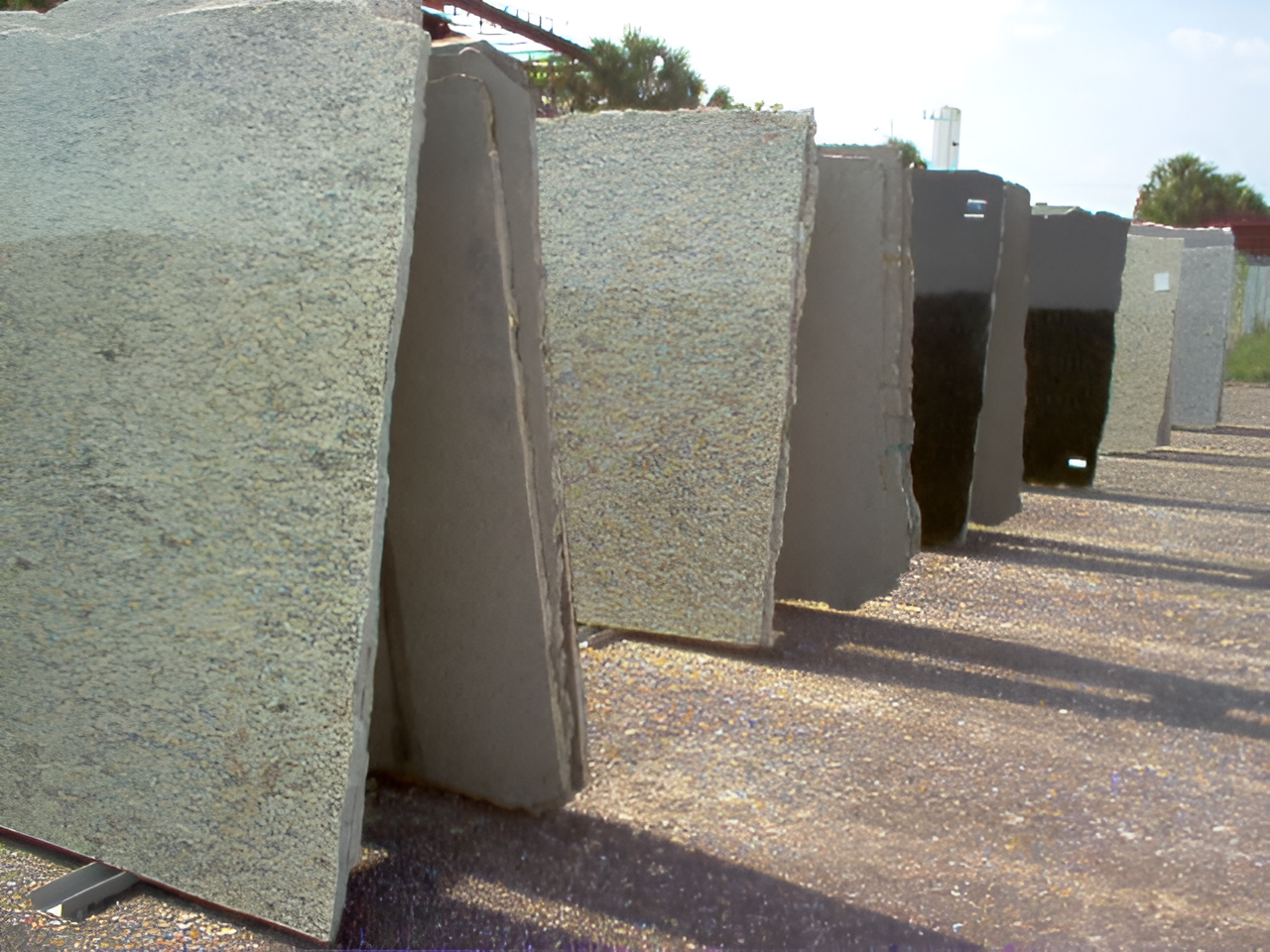 Granite slabs of various colors, leaning against a rack outdoors.