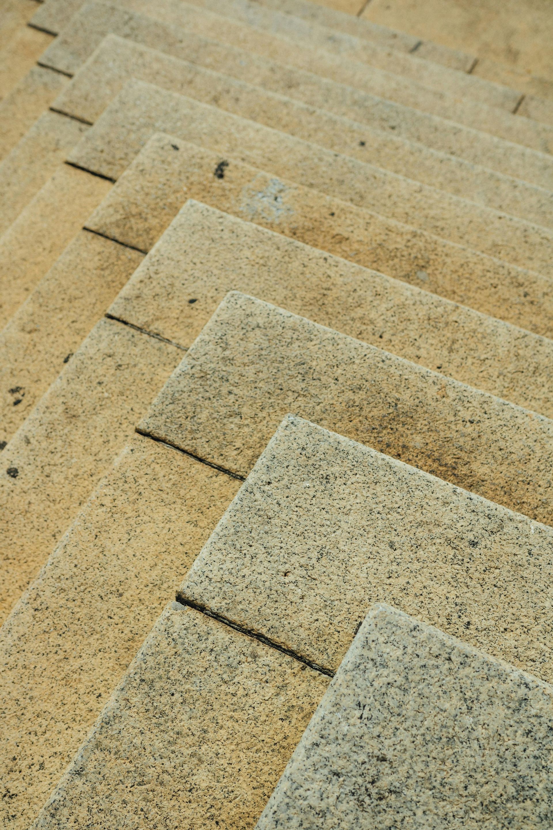 Close-up of stone steps, angled view. Beige and gray speckled texture, sunlight, outdoor setting.