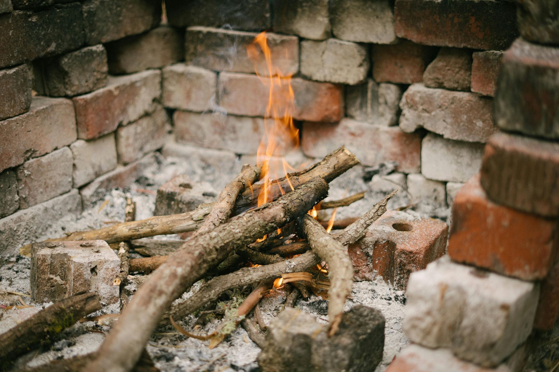 Fire burning in a brick fire pit, with orange flames and grey ash.