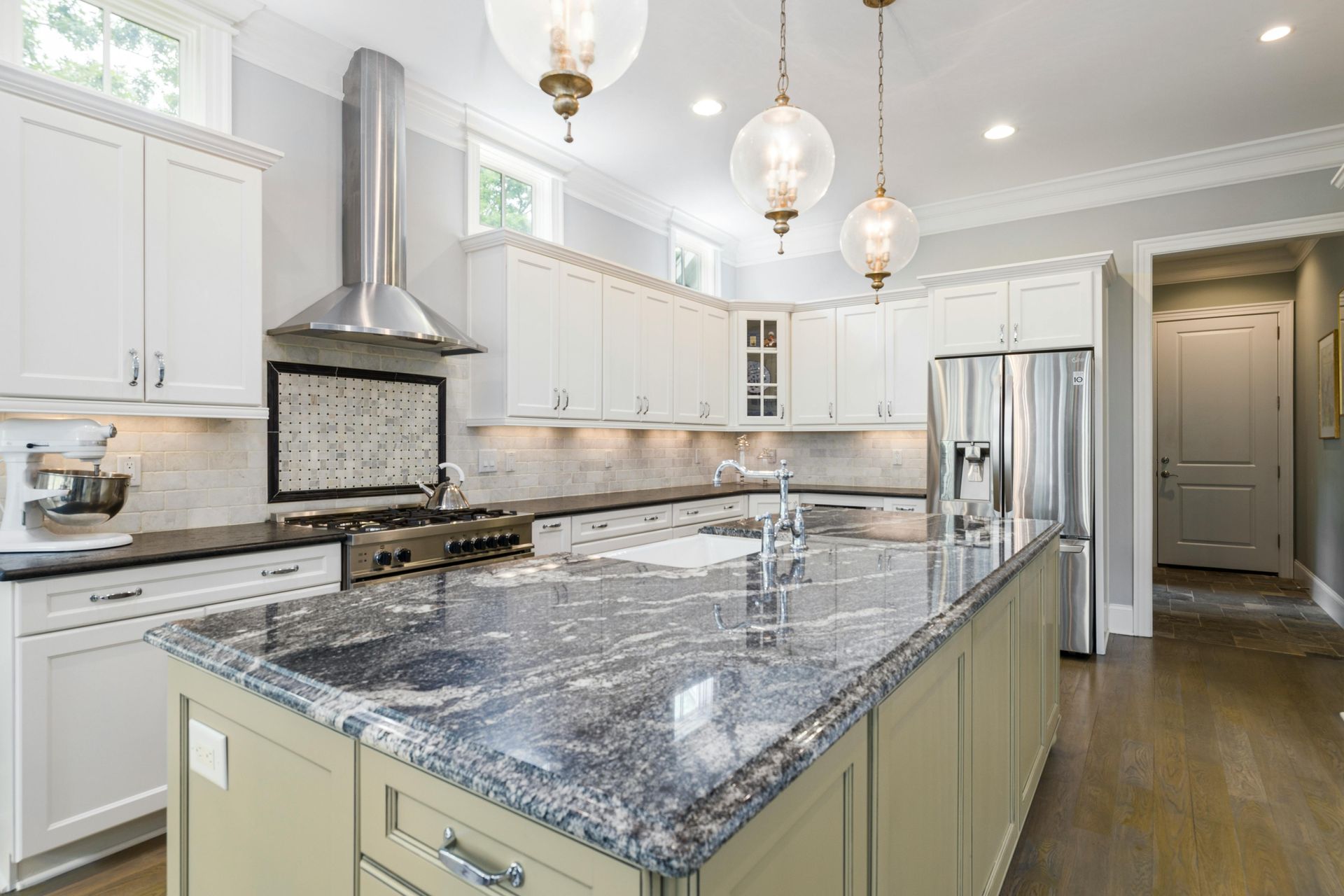 A kitchen with a large island, stainless steel appliances, white cabinets, and gray countertops.