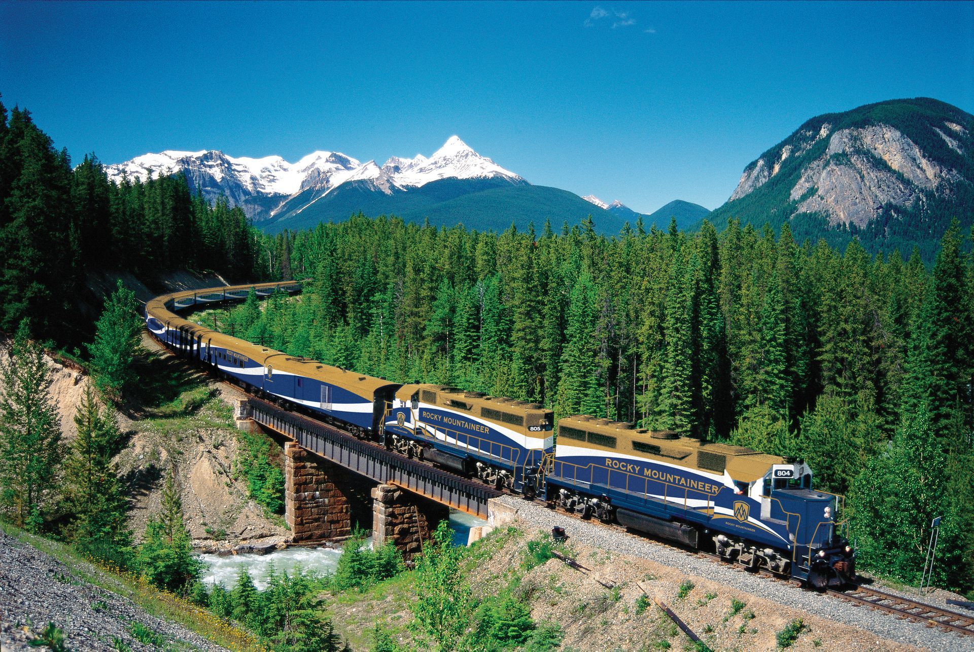 A train is going over a bridge with mountains in the background