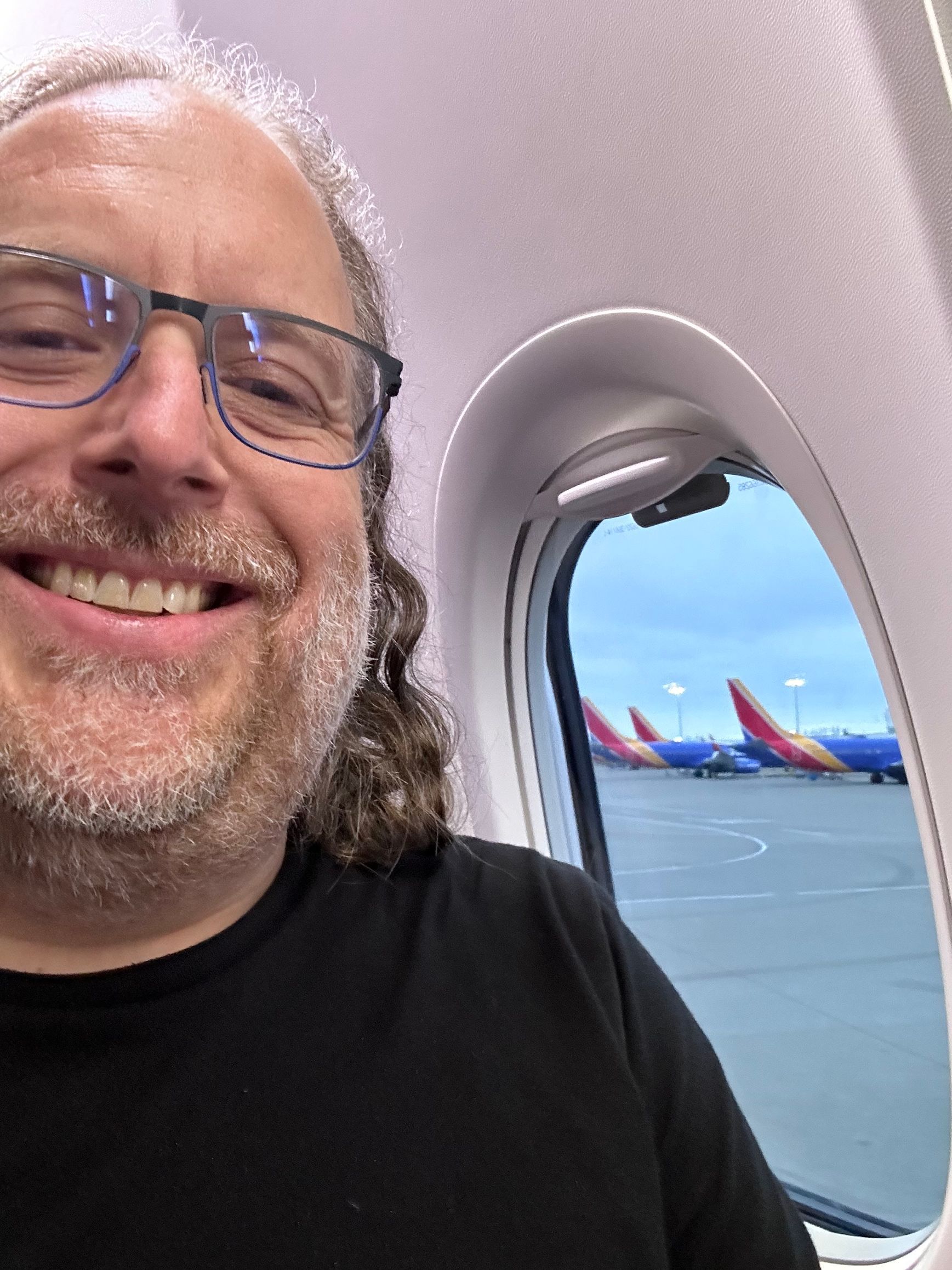 A man wearing glasses is taking a selfie on an airplane.