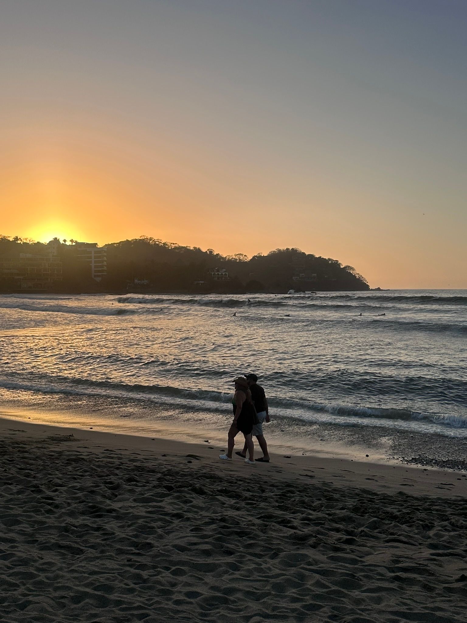 A couple is walking on the beach at sunset.