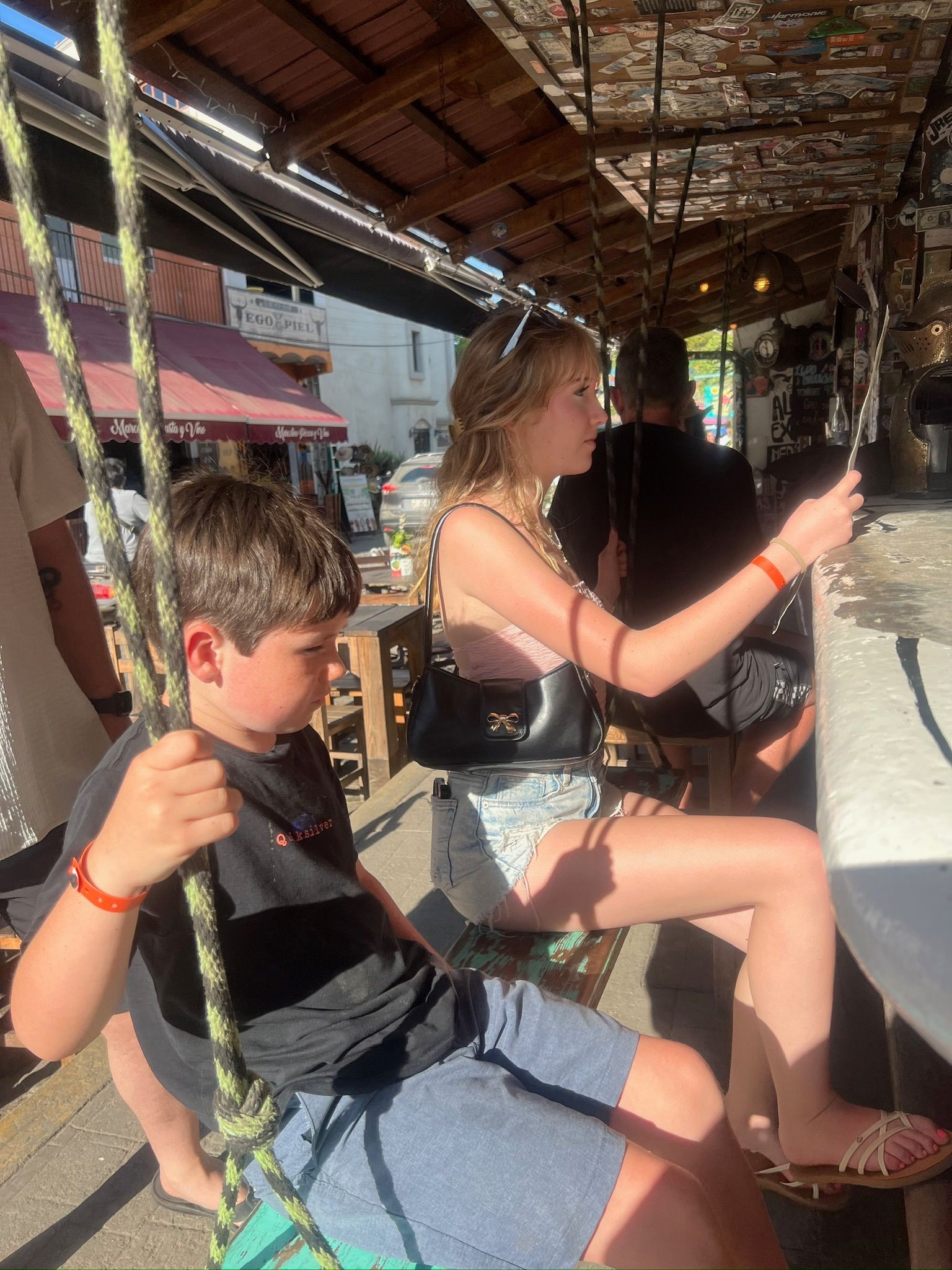 A boy and a girl are sitting on a swing looking at their phones.