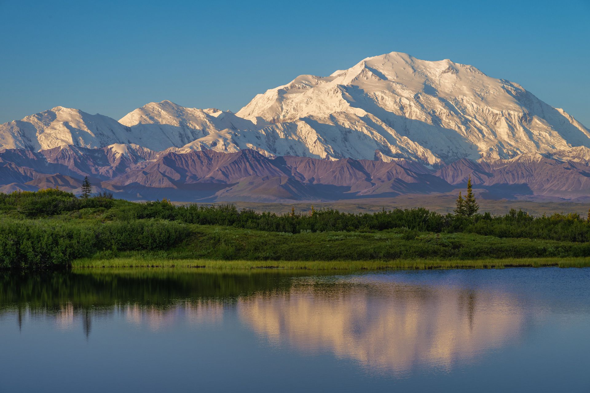 A mountain is reflected in a lake with trees in the foreground.