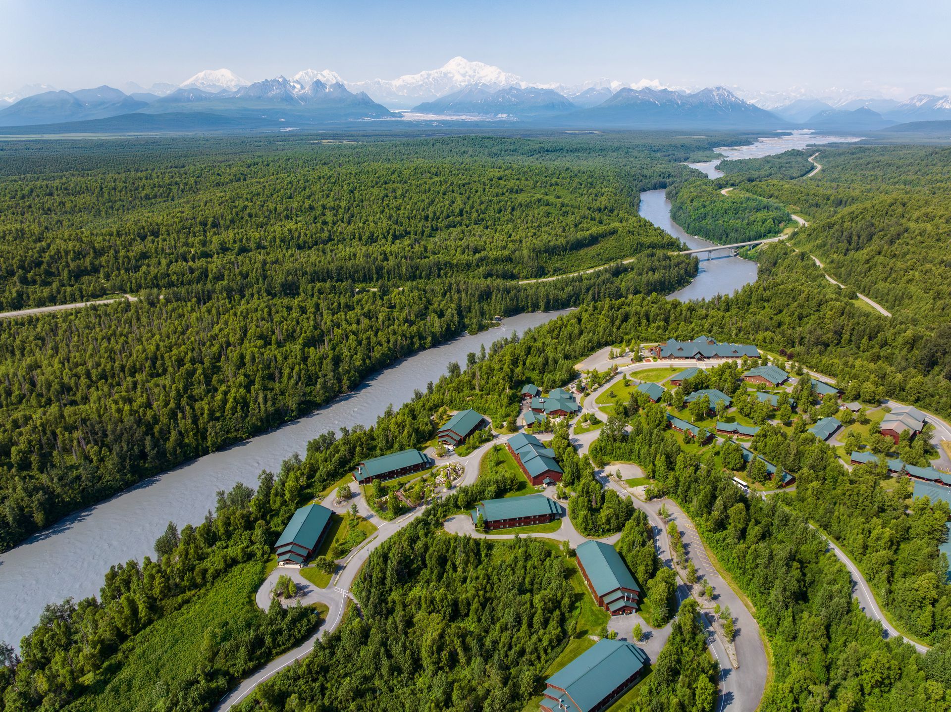 An aerial view of a river running through a lush green forest with mountains in the background.