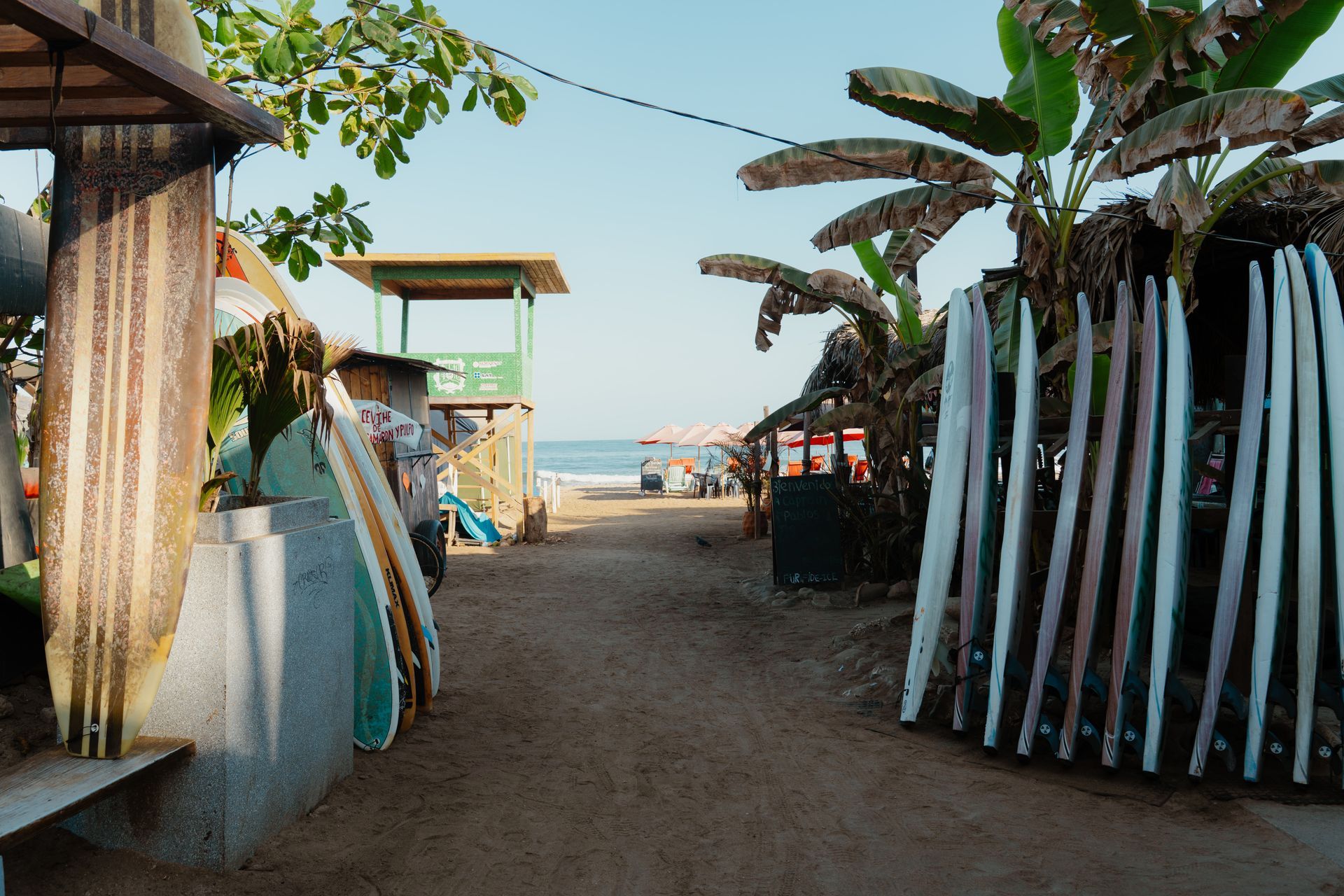 A row of surfboards are lined up on a beach next to a lifeguard tower.