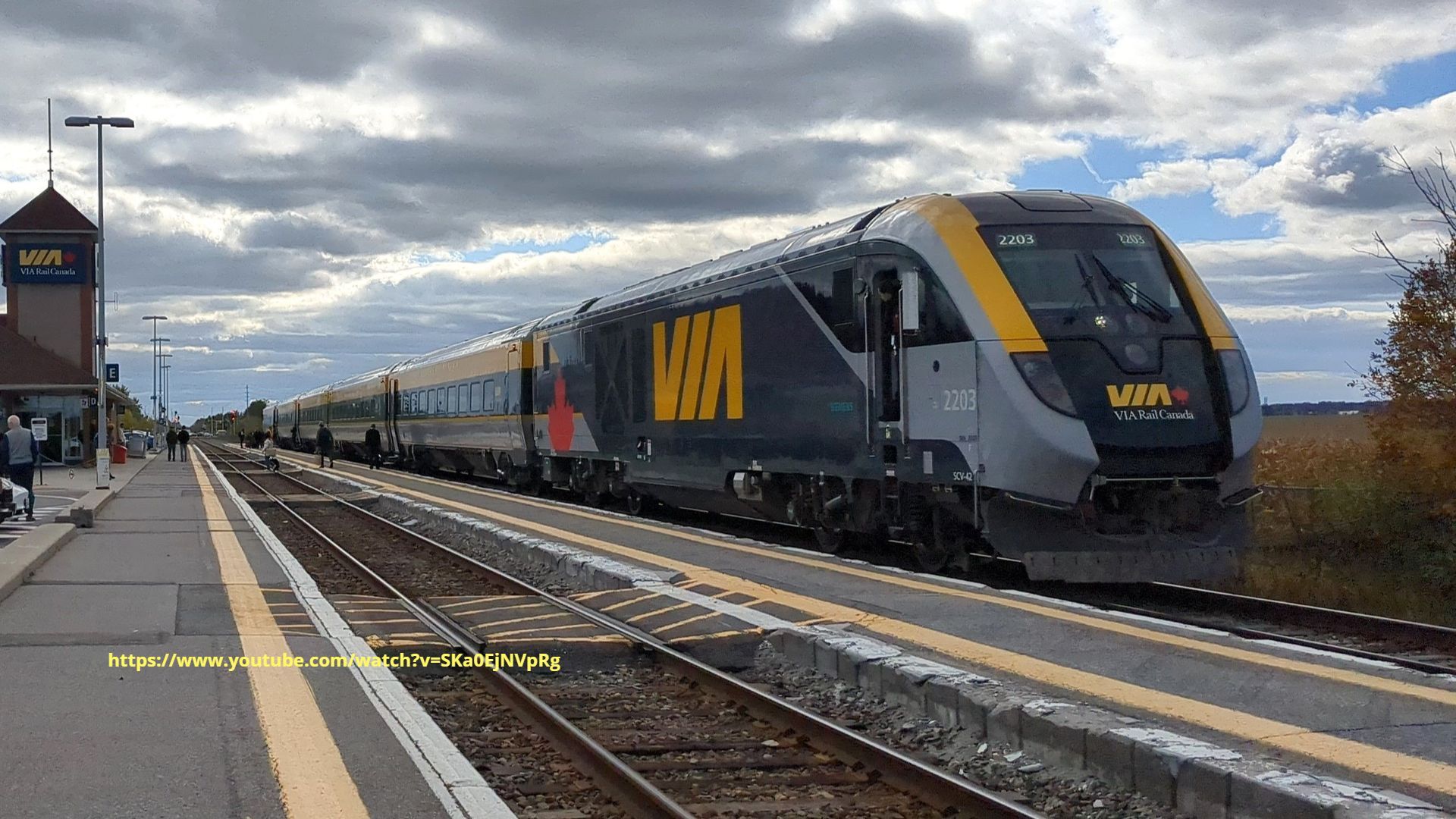A train is pulling into a train station on a cloudy day.