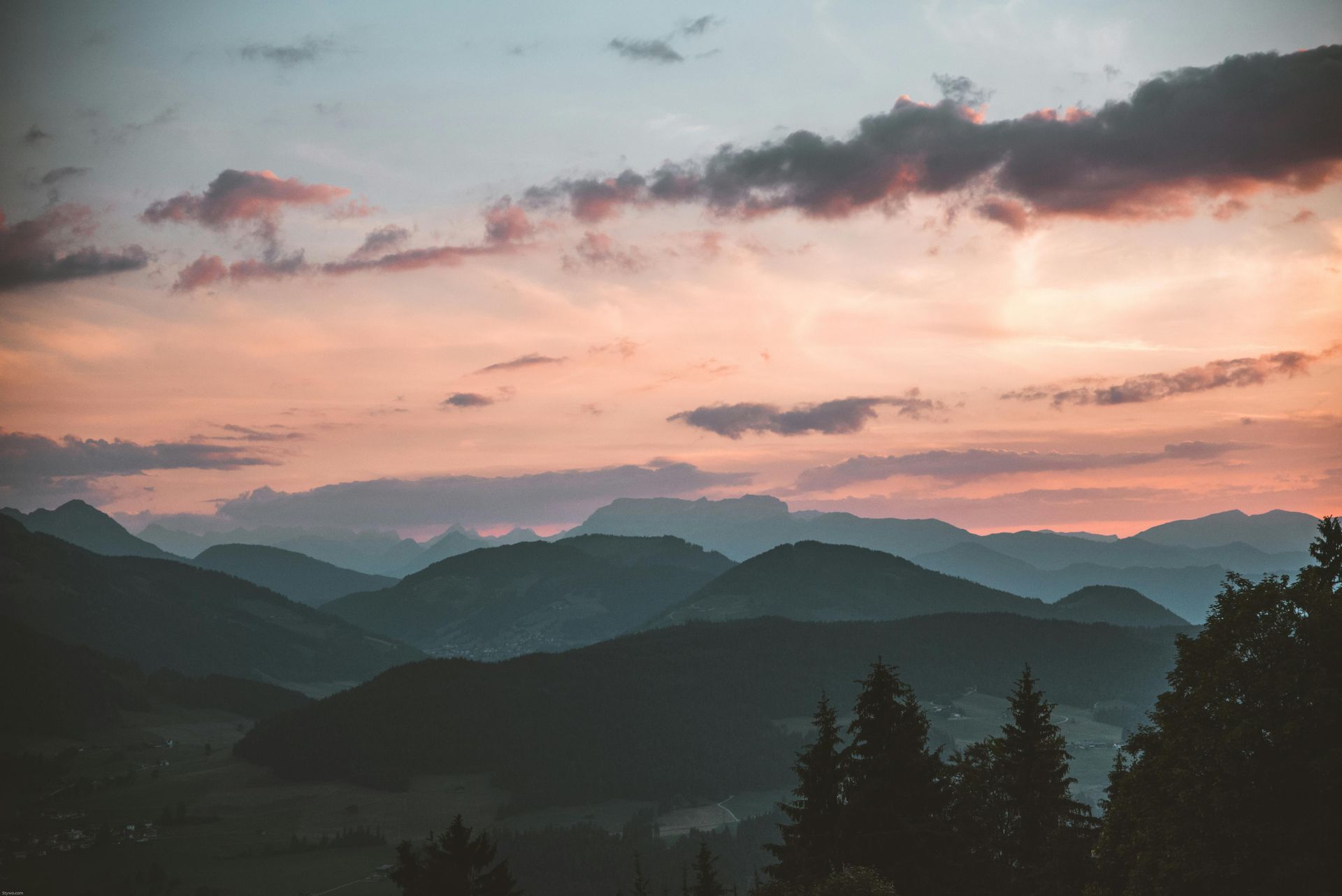 A sunset over a mountain range with trees in the foreground.