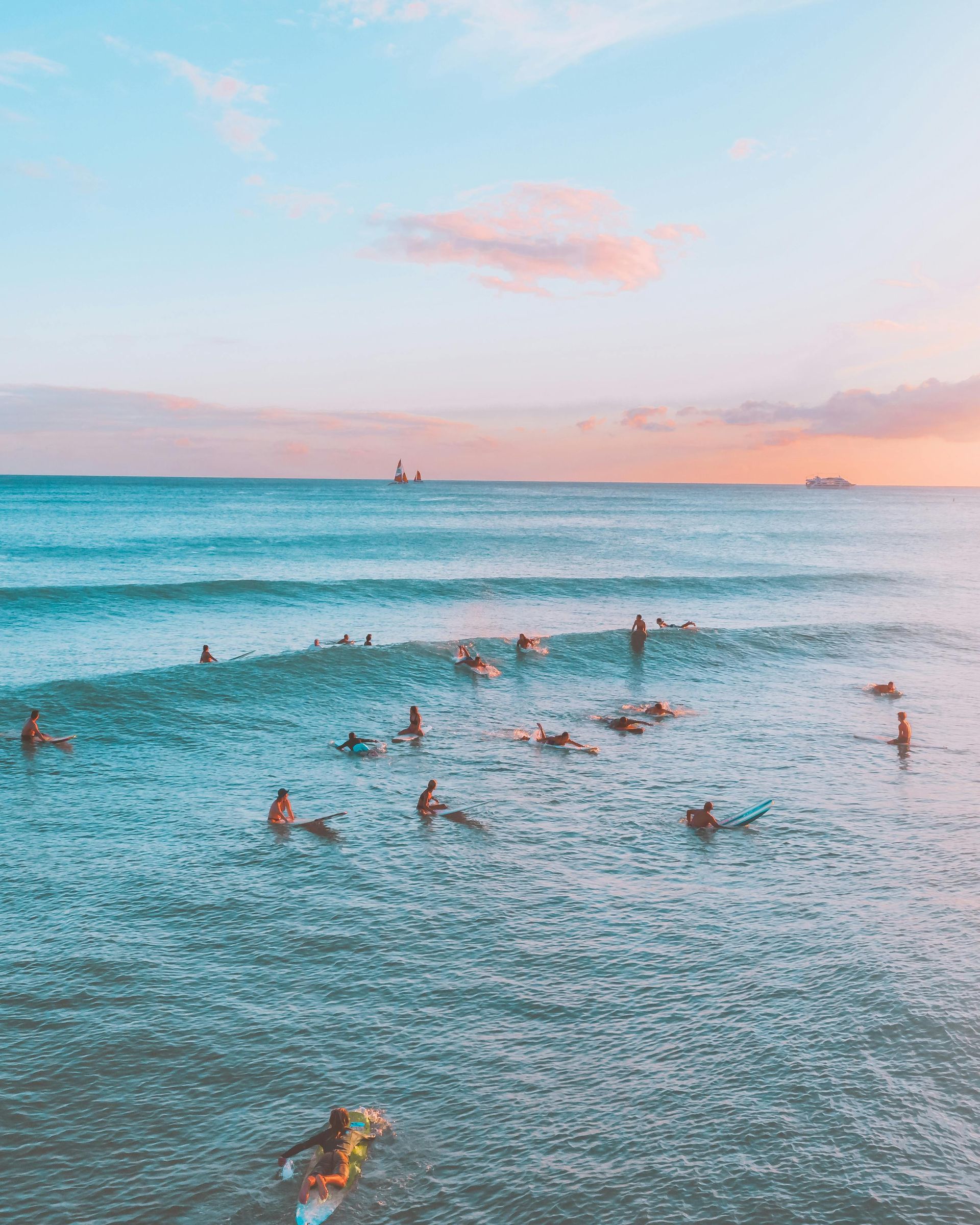 A group of people are surfing in the ocean at sunset.