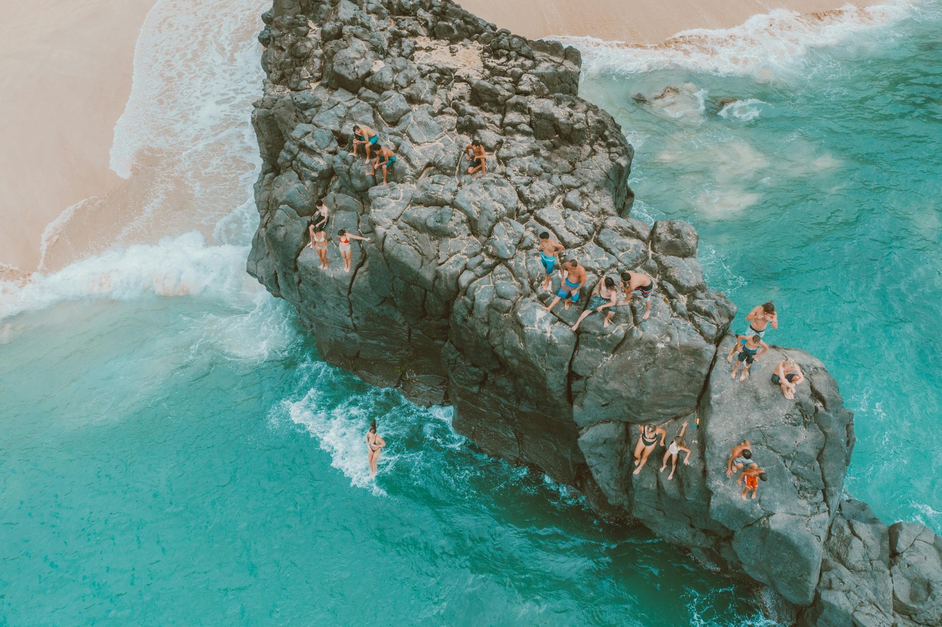 A group of people are standing on top of a large rock in the ocean.