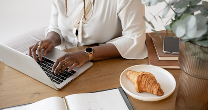 A woman is sitting at a table typing on a laptop computer.