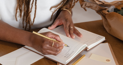 A woman is writing in a notebook with a pen.