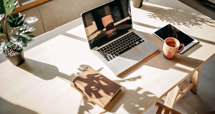 A laptop computer is sitting on top of a wooden table next to a cup of coffee.