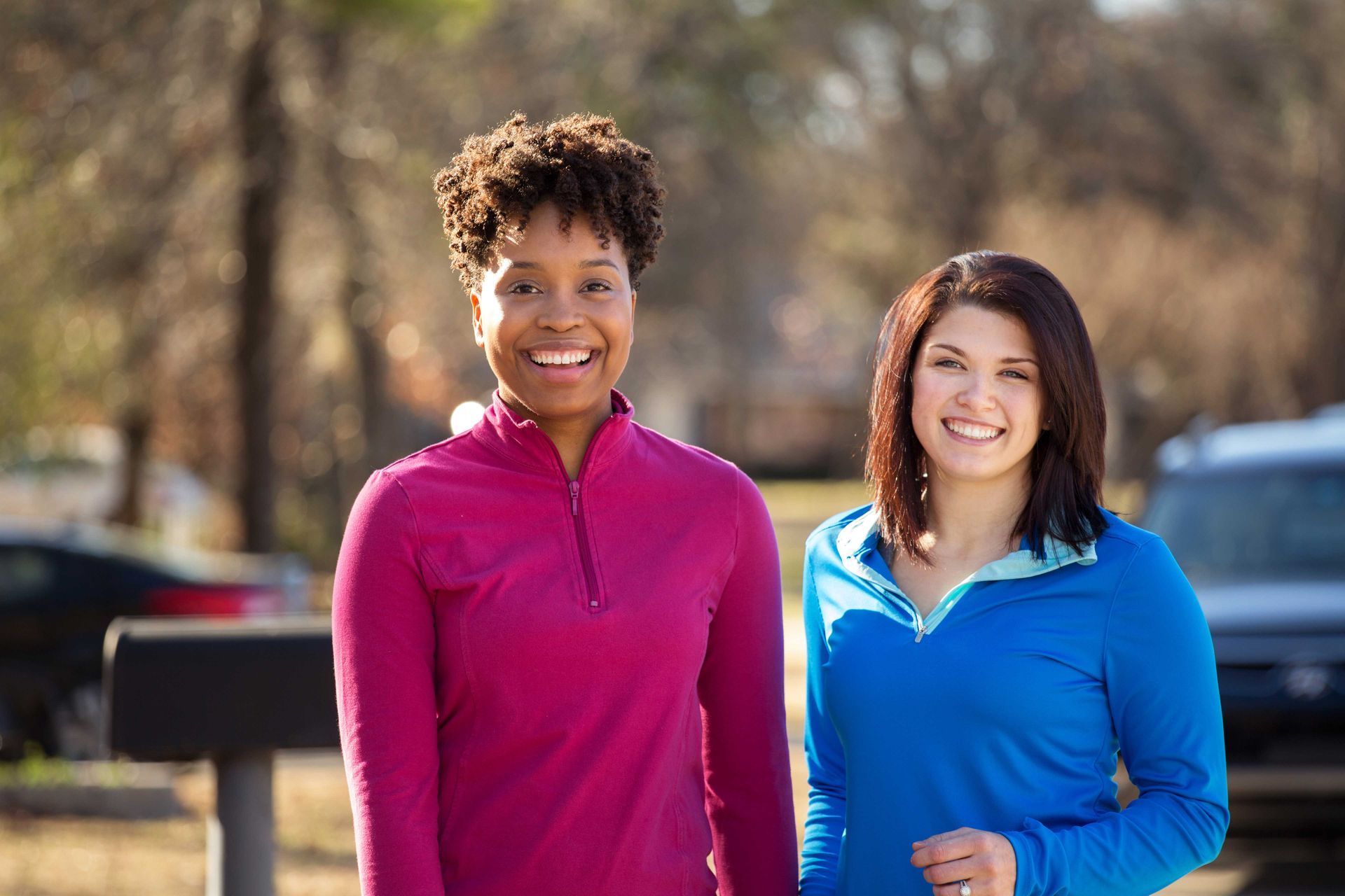 Two women smiling outdoors in athletic wear.