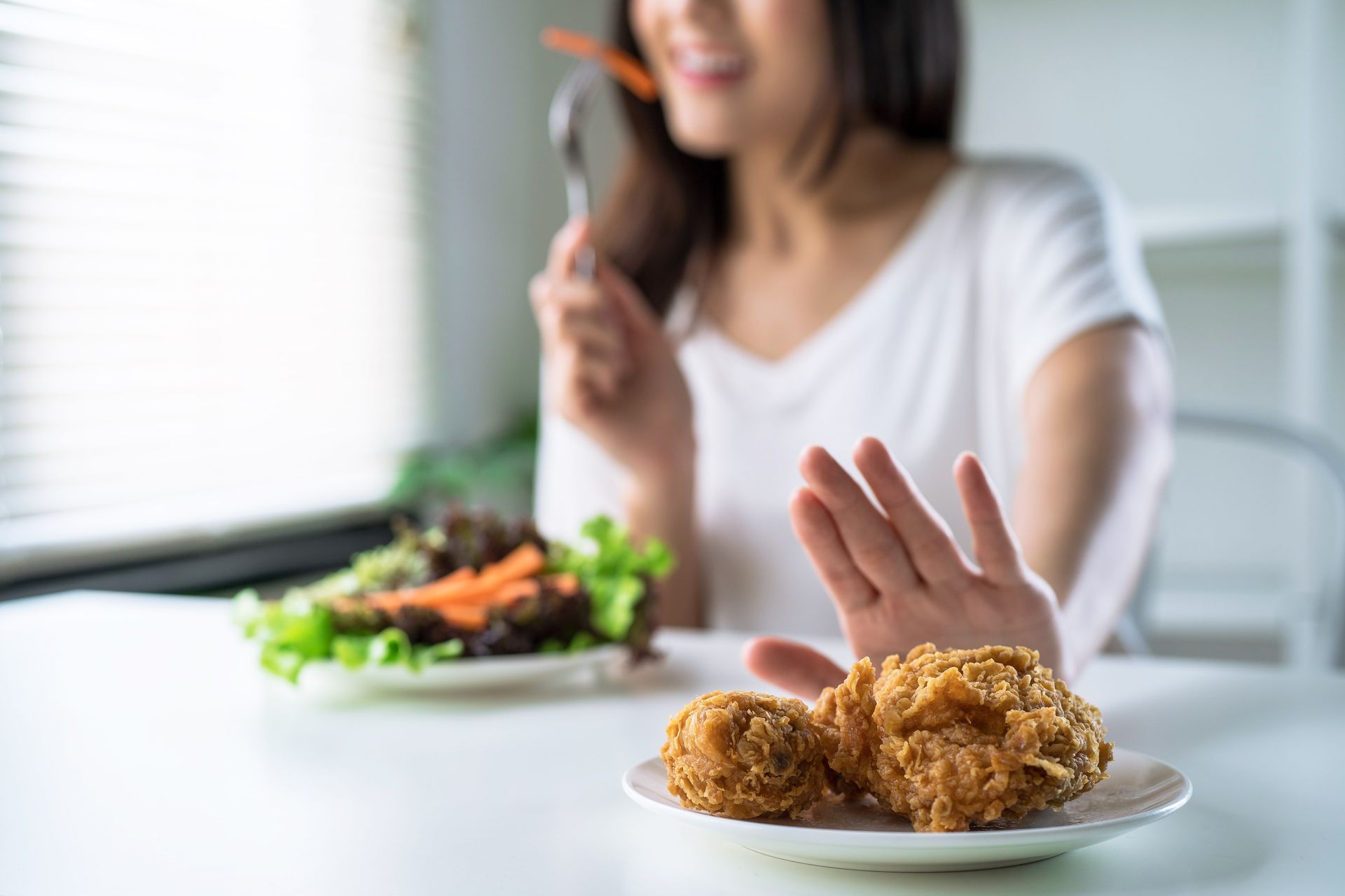 Woman gestures no to fried chicken, opting for salad.