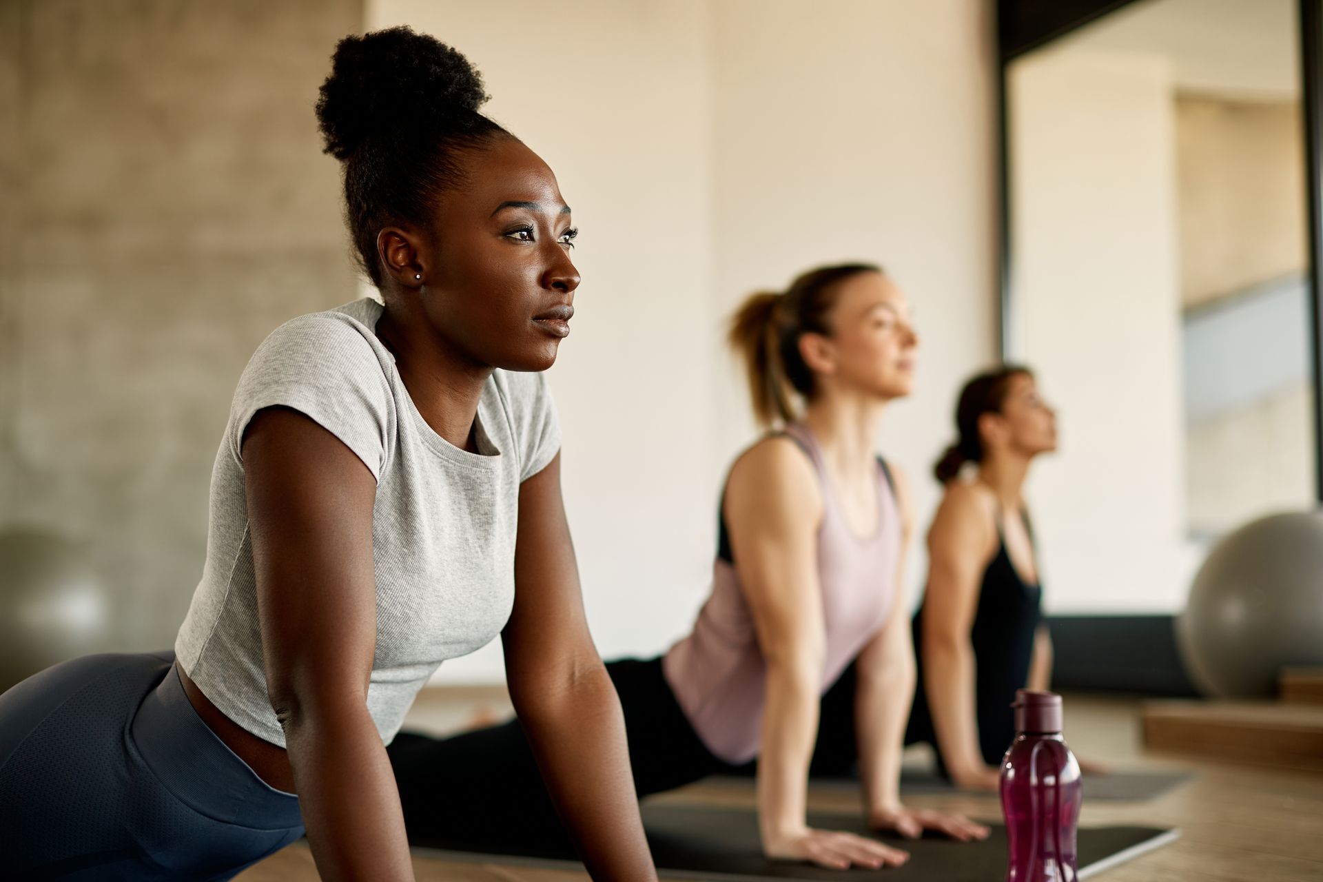 People in yoga class doing upward-facing dog pose, with mats and water bottle indoors. People in yoga class doing upward-facing dog pose, with mats and water bottle indoors.