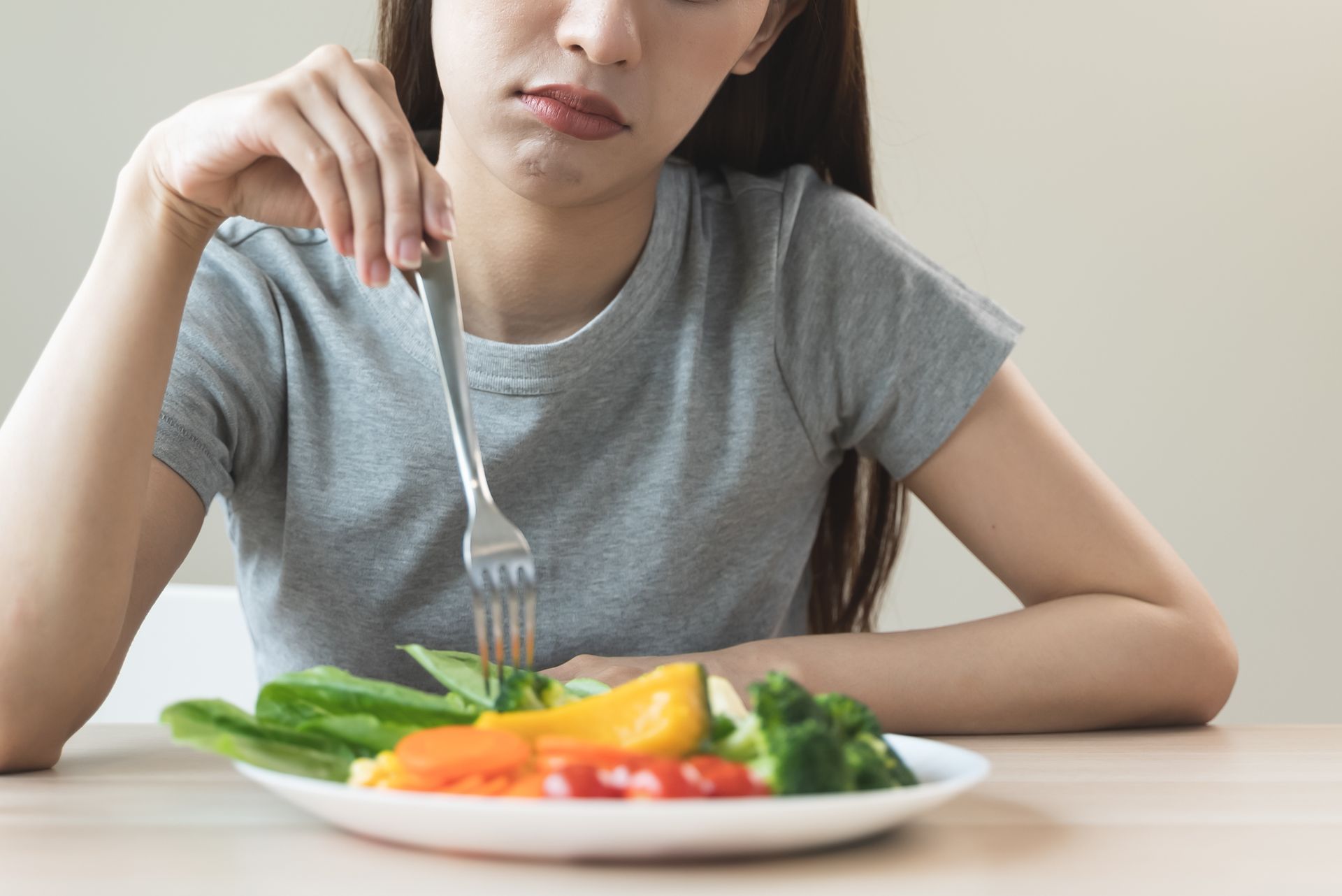 Woman with a displeased expression, looking at a plate of vegetables on a table.