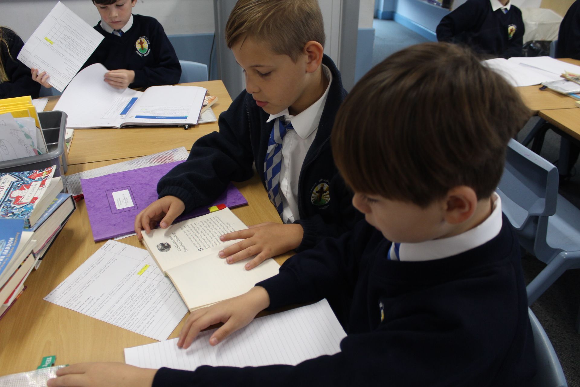 Girl in blue shirt leaning over a boy in white, both looking at a notebook on a desk.