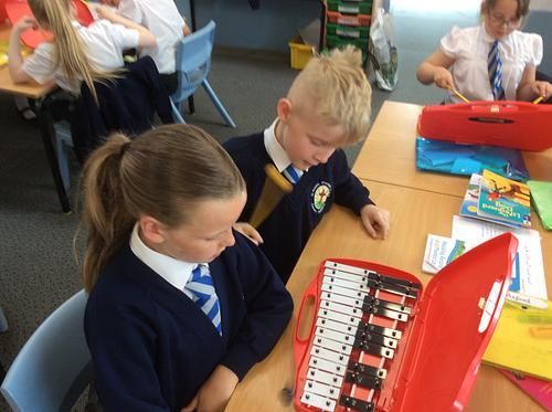 A group of children are sitting at a table in a classroom playing a musical instrument.