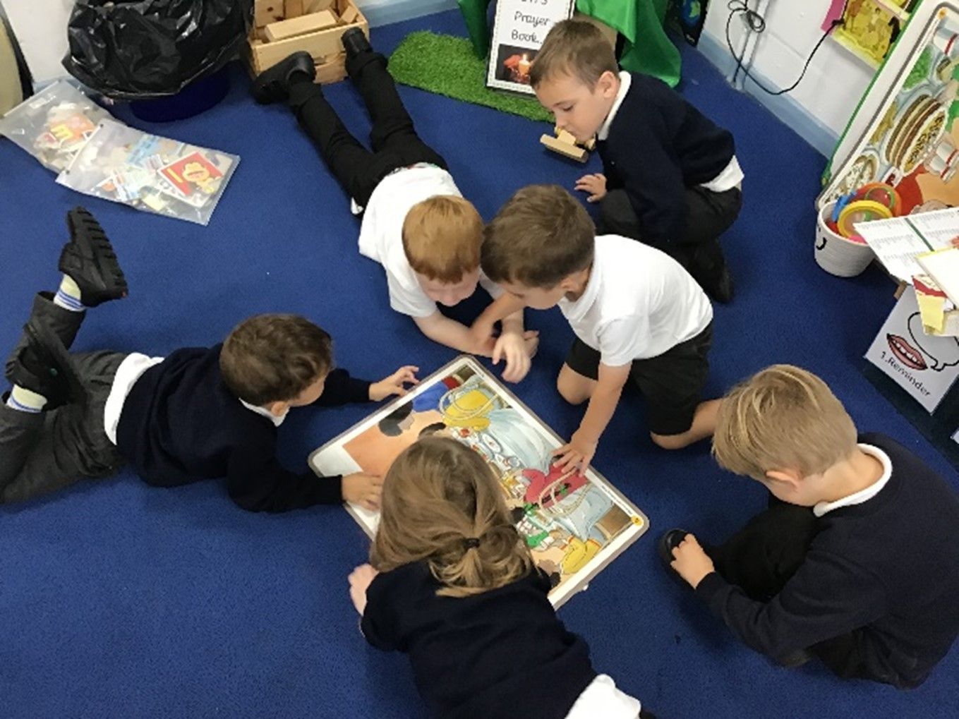 A group of children are laying on the floor reading a book.