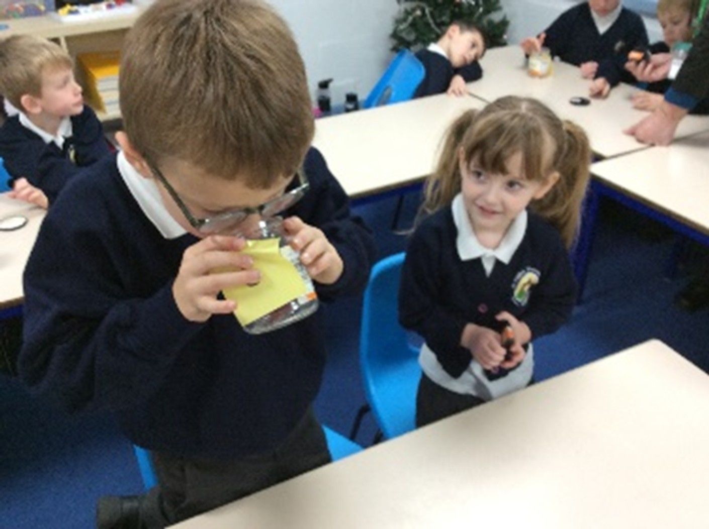 A boy is smelling something in a glass while a girl looks on