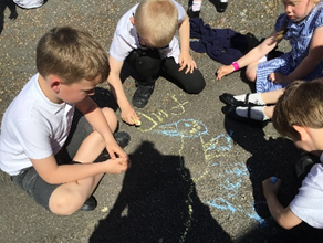 A group of children are sitting in a circle writing with chalk on the ground