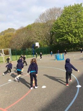 Children playing tag on an outdoor school playground, with cones and a basketball hoop nearby.