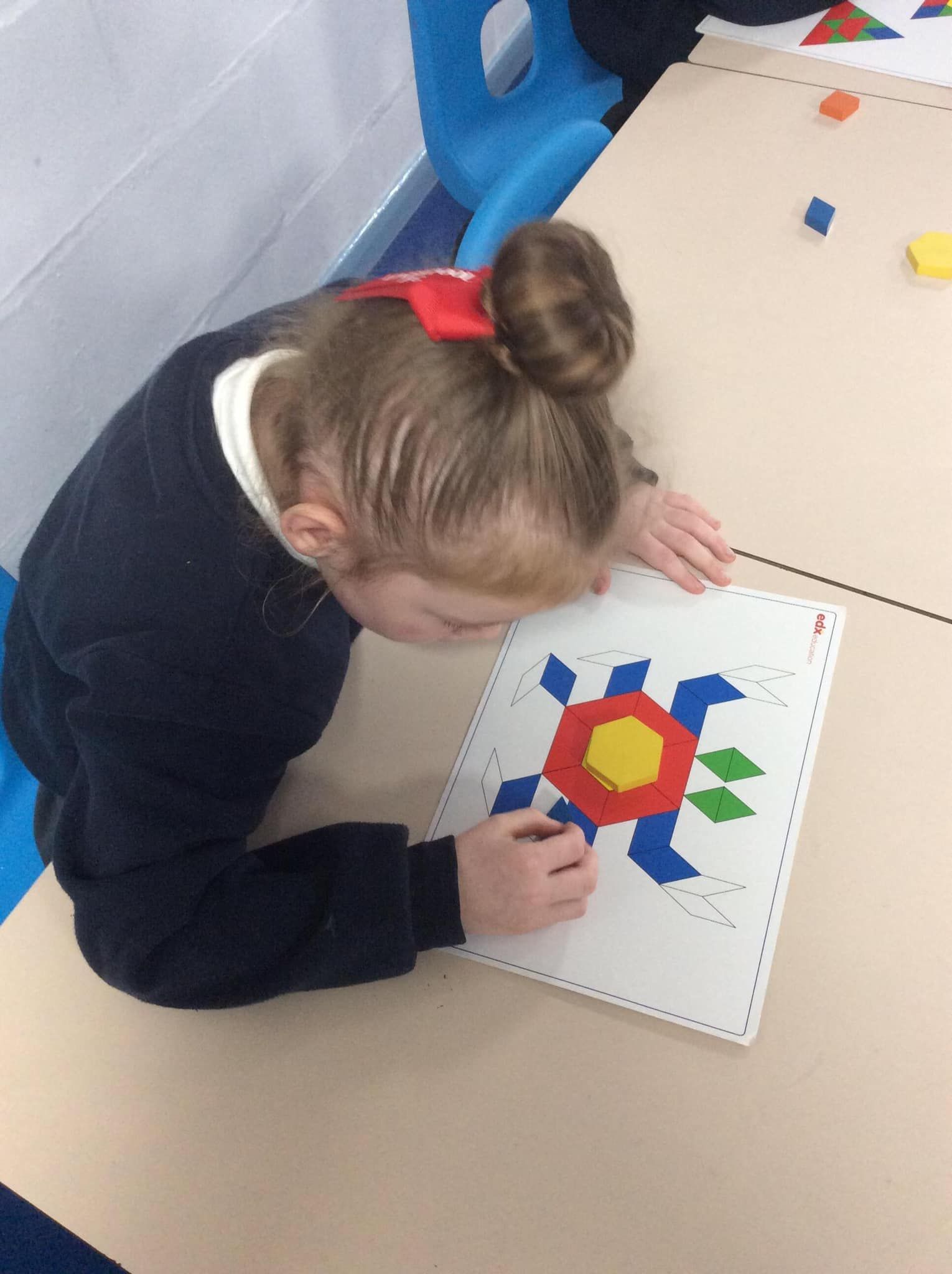 A person works on a colorful geometric pattern board with various shapes on a tabletop.