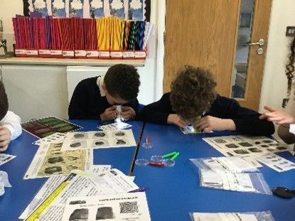 People leaning over a blue table, closely examining and drawing on papers in a classroom setting