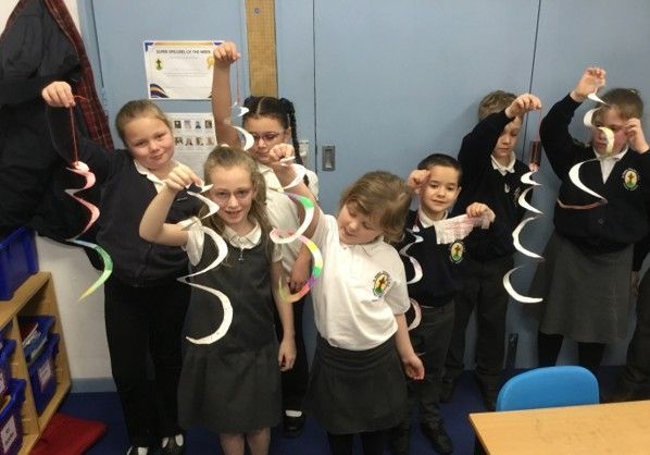 Children in uniforms holding up colorful paper spirals in a classroom.