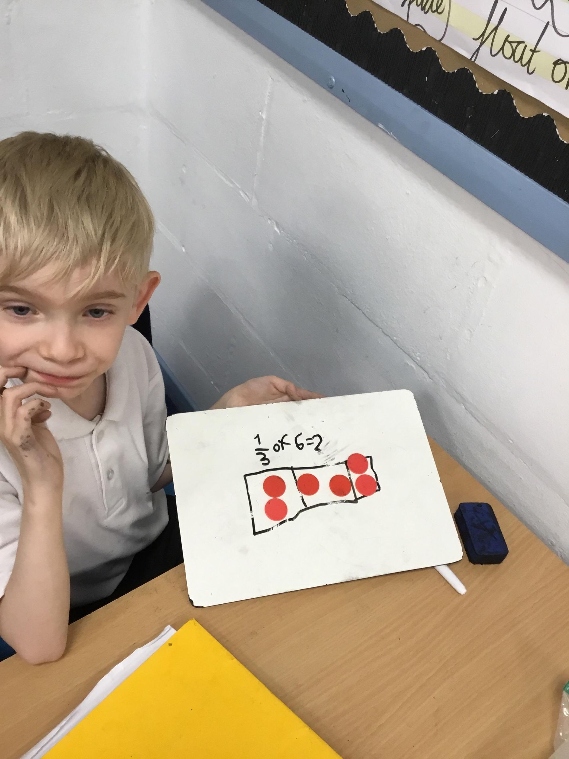 A young boy sits at a desk with a piece of paper that says 2 of 62