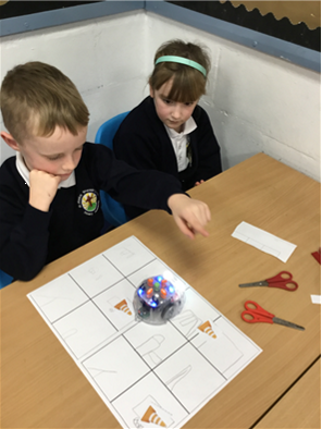 A boy and a girl sit at a table playing with a robot