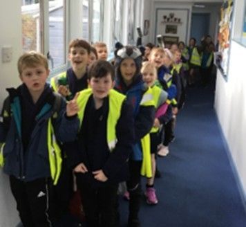 A group of children wearing yellow vests are walking down a hallway