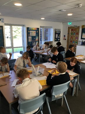 Children in school uniforms work at desks in a classroom.