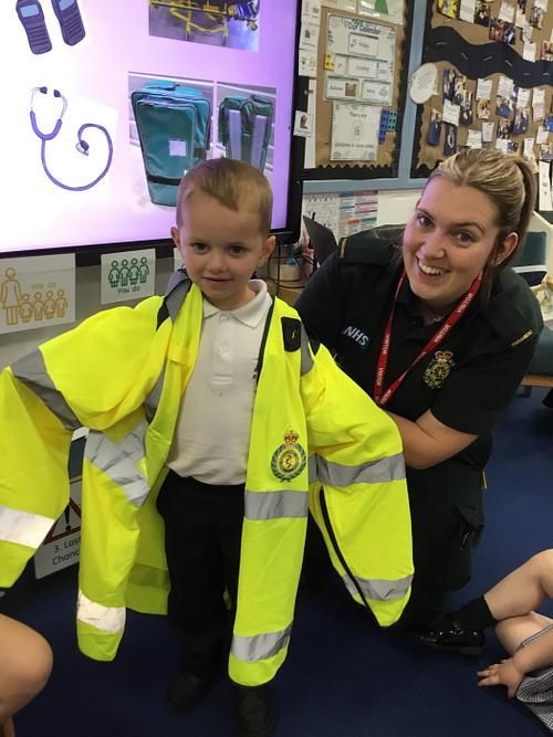 Young child in oversized yellow jacket, smiles with a medical professional. Classroom setting.