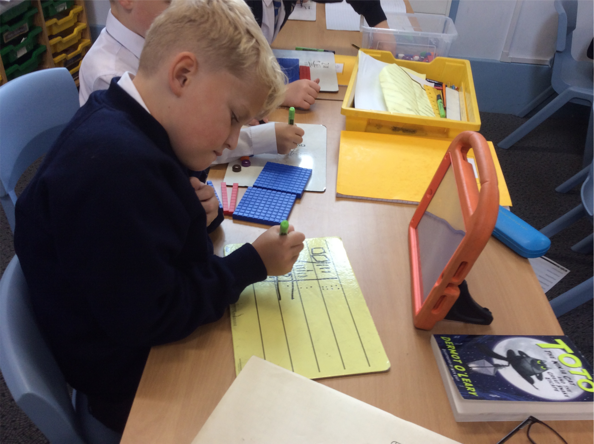 A boy is writing on a piece of paper next to a book